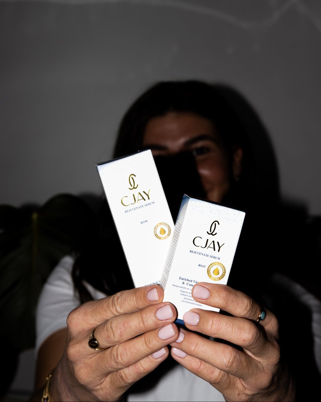Person holding two CJAY skincare products against a dark background